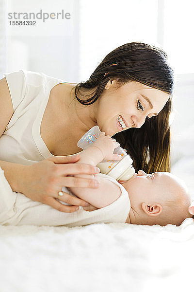 Mutter beobachtet ihren kleinen Jungen beim Trinken von Milch aus der Flasche