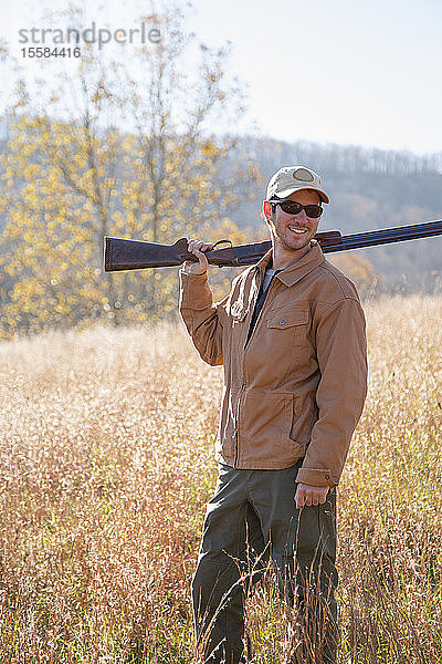 Lächelnder junger Mann mit Gewehr im Feld