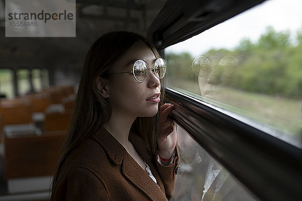 Junge Frau mit Brille schaut aus dem Zugfenster