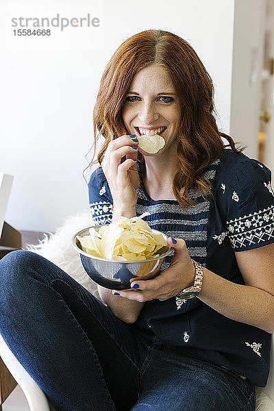 Lächelnde Frau isst Chips aus einer Schüssel