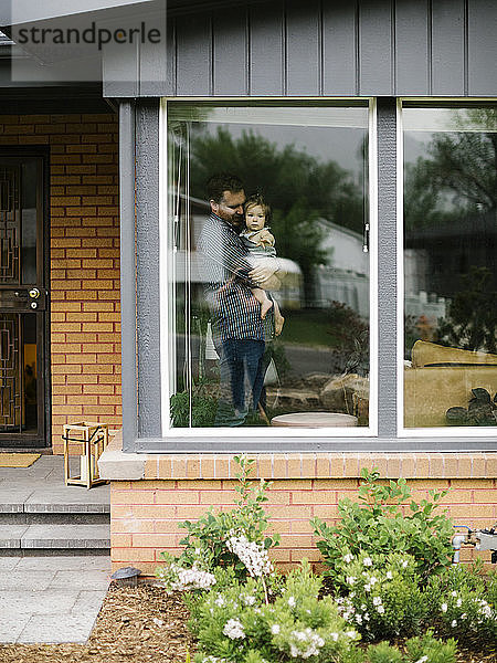 Vater hält seine Tochter hinter dem Fenster eines Hauses