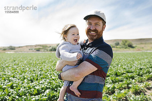 Lächelnder Vater hält kleines Mädchen in einem Getreidefeld
