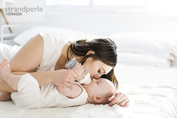 Mutter küsst ihren Sohn auf die Wange  während er eine Flasche Milch trinkt