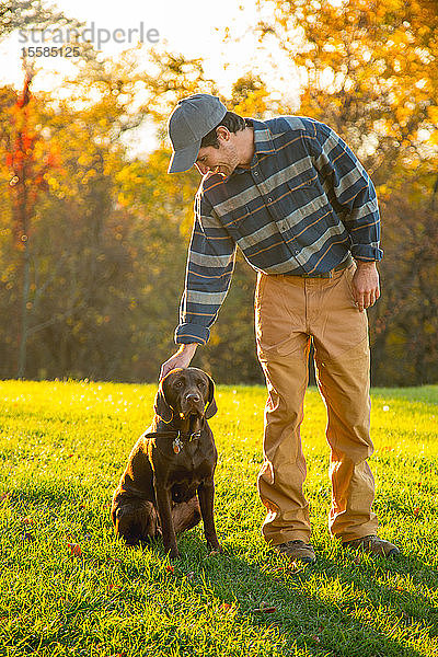 Mann streichelt schokoladenfarbenen Labrador auf einem Feld im Herbst