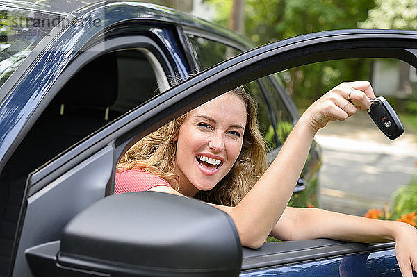 Lächelnde junge Frau im Auto mit Autoschlüssel