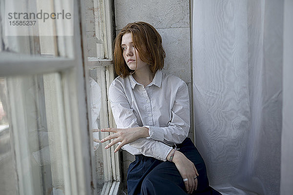 Junge Frau mit weißem Hemd auf dem Fensterbrett
