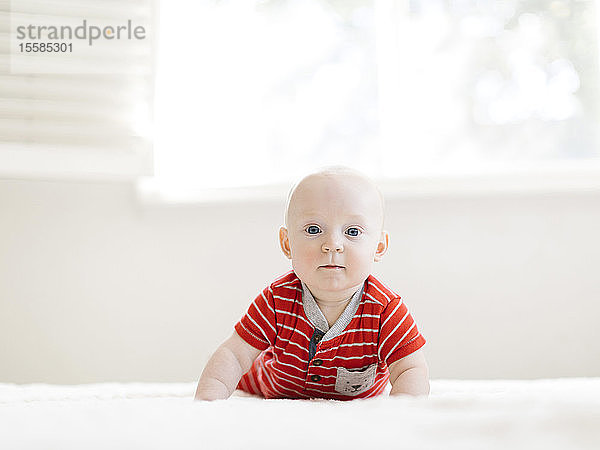 Baby-Junge trägt gestreiften Strampler auf dem Bett
