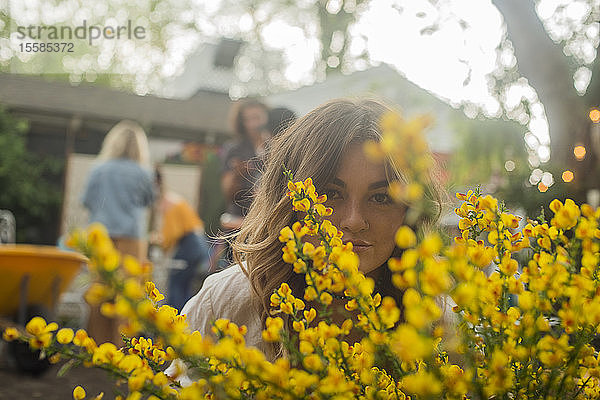 Junge Frau versteckt sich hinter gelber Blüte auf Gartenparty der Gemeinde  Kopf- und Schulterporträt