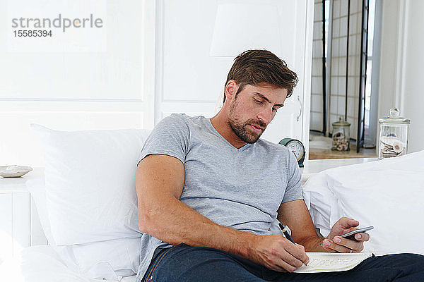 Mann benutzt Smartphone und schreibt Notizen auf dem Sofa