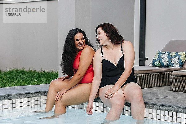 Zwei mittelgroße erwachsene Frauen sitzen am Swimmingpool im Freien und unterhalten sich und lachen miteinander  Kapstadt  Südafrika