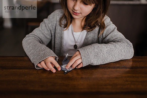 Mädchen am Tisch faltet Papier  macht Origami  Kopf und Schultern