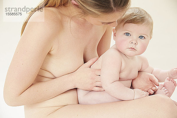 Nackte Mutter bindet mit nacktem Baby auf dem Schoß