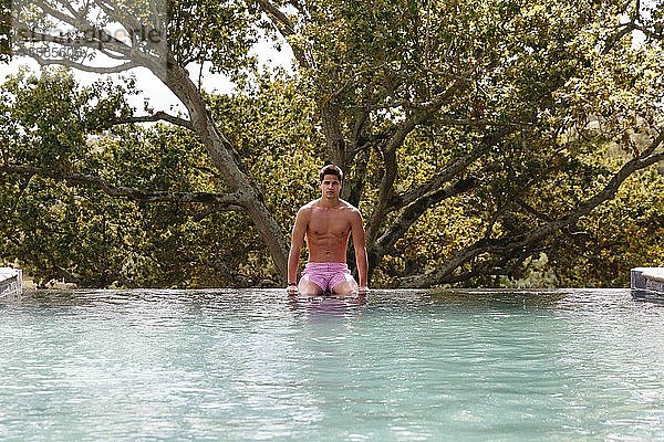 Am Rand eines Schwimmbeckens sitzender Mann mit Beinen im Wasser