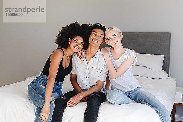 Glücklicher junger Mann und zwei Freundinnen sitzen auf dem Bett  Porträt