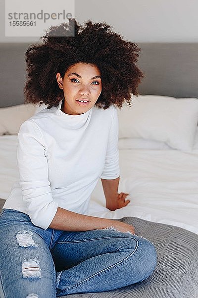 Junge Frau mit Afrofrisur auf Bett sitzend  Porträt