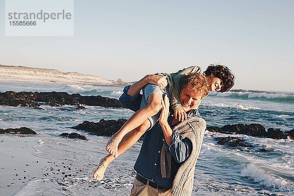 Vater trägt Sohn am Strand über die Schulter