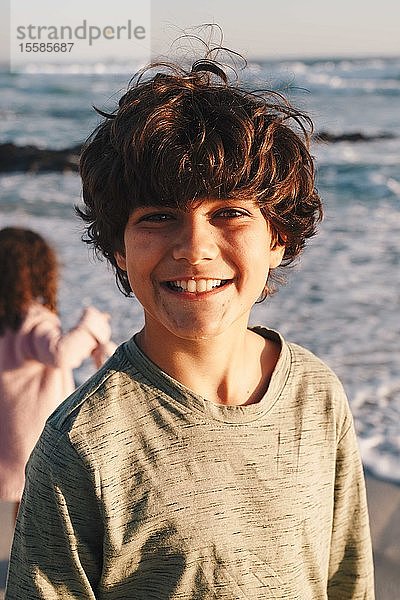 Junge lächelt am Strand  Schwester im Hintergrund