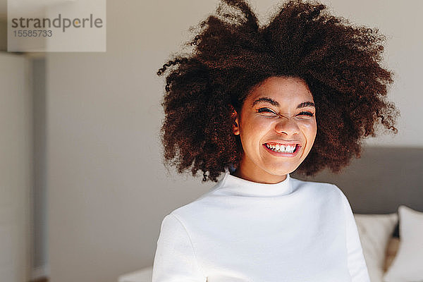 Junge Frau mit Afrofrisur lacht im Schlafzimmer  Kopf- und Schulterporträt