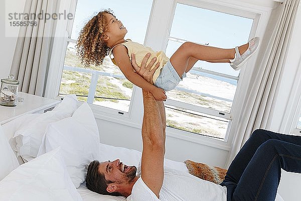 Vater hebt Tochter in der Luft auf Bett im Strandhaus