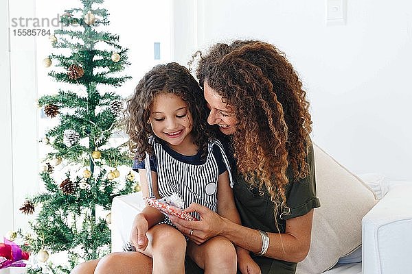 Mutter schenkt Tochter zu Hause neben dem Weihnachtsbaum
