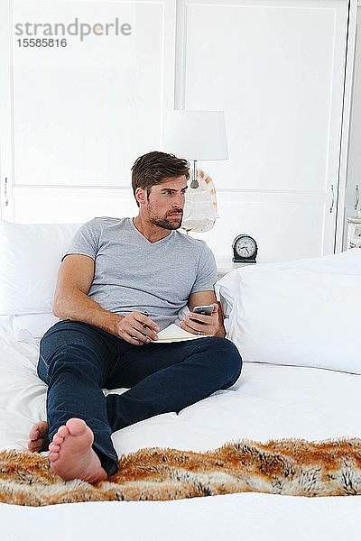 Mann benutzt Smartphone und schreibt Notizen auf dem Sofa