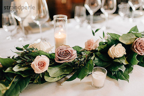 Gedeck am Hochzeitstisch mit Rosengirlandendekoration  Kerzen und Trinkgläsern