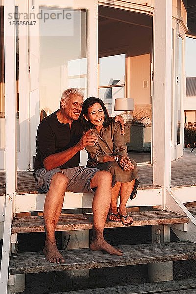 Älteres Ehepaar genießt Sonnenuntergang auf Stufen vor dem Strandhaus