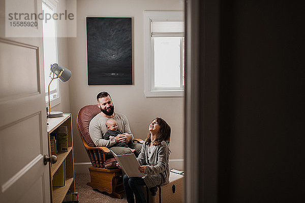 Junger Mann mit kleinem Sohn auf dem Schoß  lacht mit Tochter im Wohnzimmer