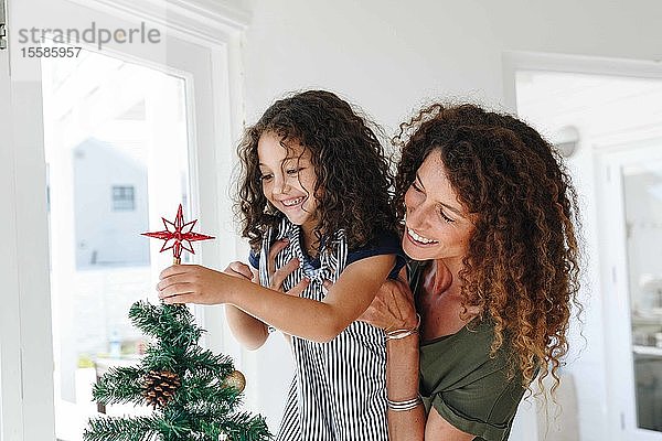 Mutter hilft Tochter  zu Hause einen Stern auf den Weihnachtsbaum zu setzen