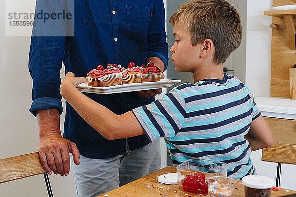 Vater serviert einem Jungen zu Hause ein Tablett mit Cupcakes