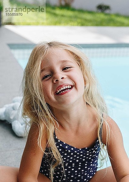 Glückliches kleines Mädchen sitzt am Swimmingpool