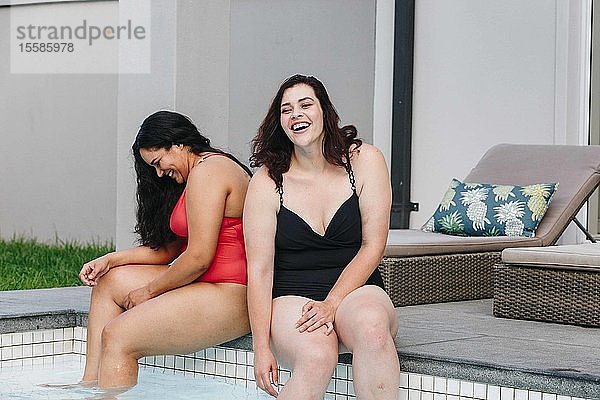 Zwei mittelgroße erwachsene Frauen sitzen zusammen lachend am Swimmingpool im Freien  Kapstadt  Südafrika