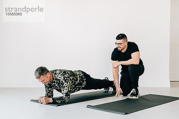 Fitnesstrainerin beobachtet Mann beim Plankenmachen im Studio