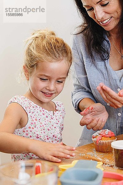 Mutter und Tochter dekorieren Cupcake mit Zuckerguss in der Küche
