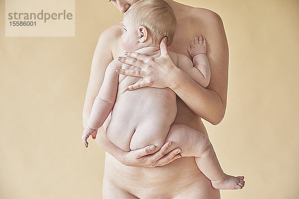 Nackte Mutter tröstet nacktes Baby  das an ihrer Brust liegt