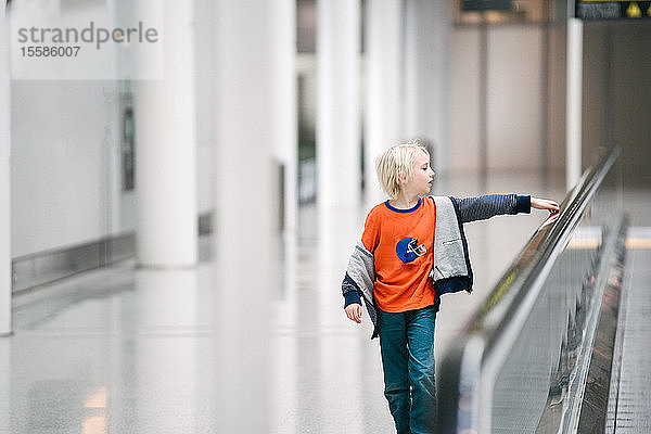 Junge mit Hand am Handlauf des Fahrsteigs im Flughafen  selektiver Fokus