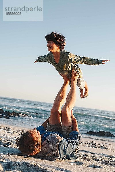 Vater hebt Sohn in der Luft mit Beinen am Strand