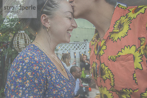 Junger Mann gibt seiner Freundin auf der Gartenparty einen Kuss auf die Stirn  Seitenansicht beschnitten