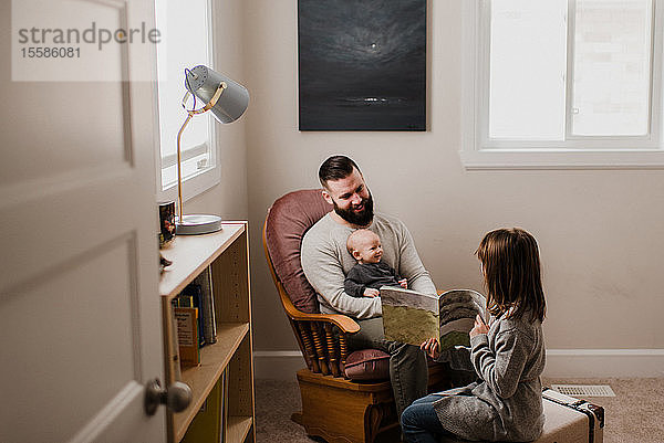Mädchen im Wohnzimmer zeigt dem Vater und dem kleinen Bruder ein Buch