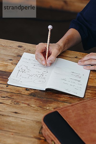 Frau schreibt in Notizbuch auf Tischplatte