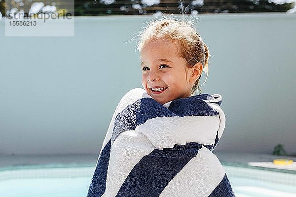 Glückliches kleines Mädchen am Swimmingpool in ein Handtuch gewickelt