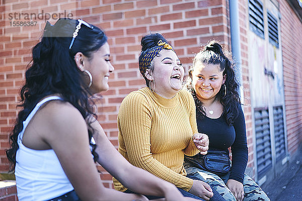 Junge Frau und ihre jugendlichen Schwestern sitzen lachend an der Wand