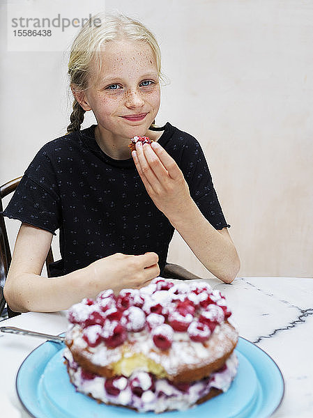 Mädchen isst ihren selbstgebackenen Kuchen mit frischen Himbeeren am Küchentisch  Porträt