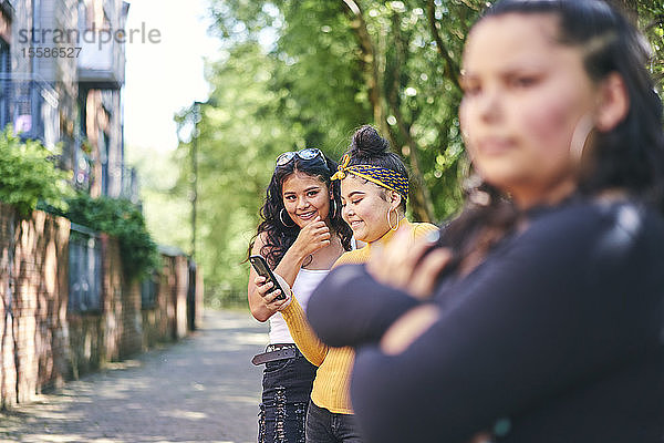 Junge Frau mit jugendlichen Schwestern beim Smartphone am Park