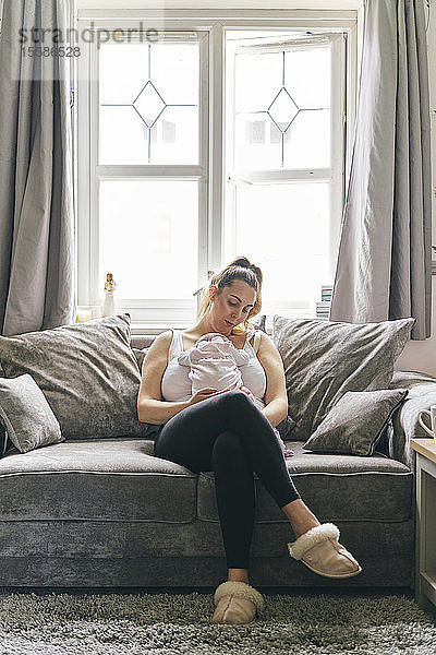 Mutter trägt Baby gegen die Brust auf dem Sofa