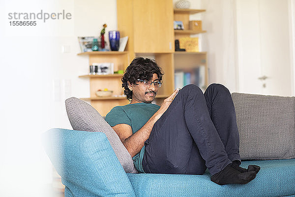 Mittelgroßer Mann entspannt sich auf dem Sofa und schaut auf ein Smartphone