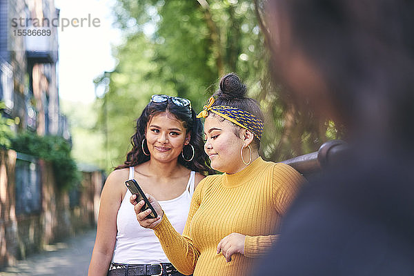 Junge Frau mit Schwestern im Teenageralter schaut auf Smartphone am Park  Blick über die Schulter