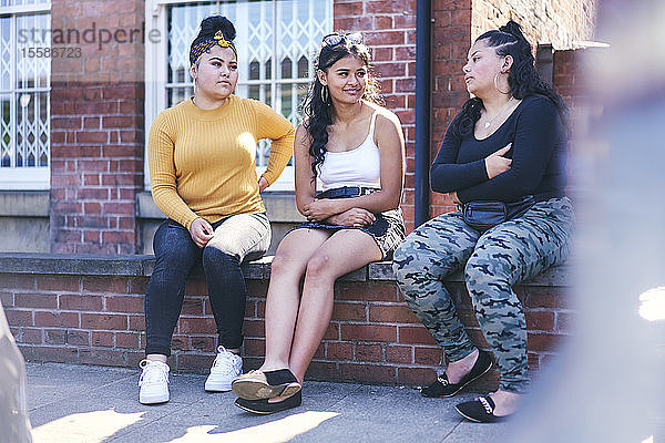 Junge Frau und ihre jugendlichen Schwestern sitzen an der Wand und unterhalten sich