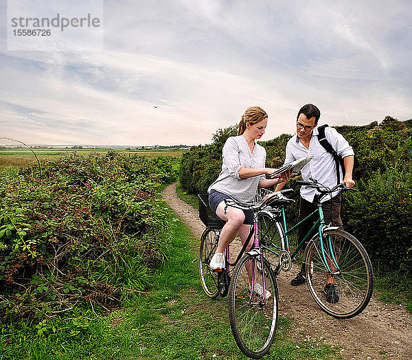 Mittleres erwachsenes Radfahrerpaar auf ländlichem Feldweg mit Blick auf die Karte  Southwold  Suffolk  UK
