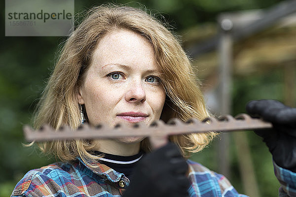 Mittlere erwachsene Frau mit Gartenharke  Kopf und Schulterporträt